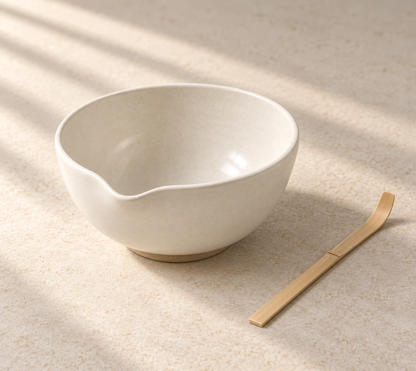 Ivory pouring bowl viewed from a low three-quarter angle, with a bamboo scoop beside it in warm window light